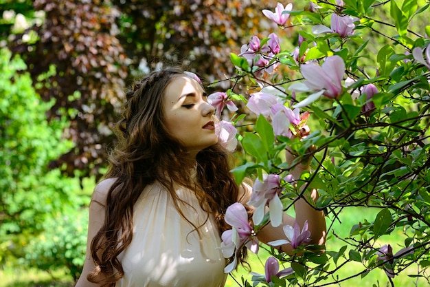Portret młodej atrakcyjnej kobiety w wiosennym ogrodzie z kwitnącymi magnoliami. Wiosna w tle