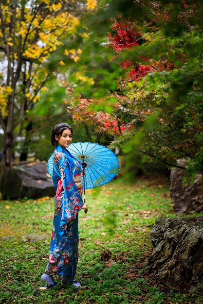 Portret młodej azjatyckiej kobiety noszącej japońskie niebieskie kimono historię mody i parasol stojący w parku w sezonie jesiennych liści w japonii