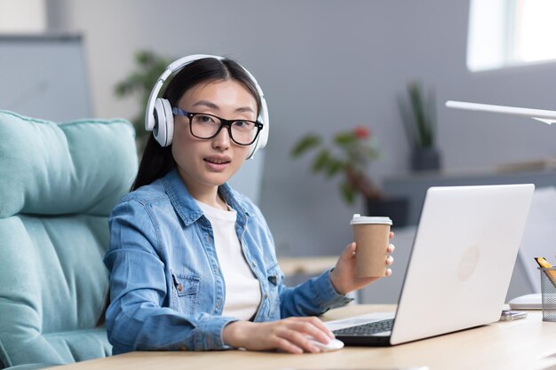 Portret młodej azjatyckiej studentki studiującej online na laptopie za pomocą laptopa i słuchawek do