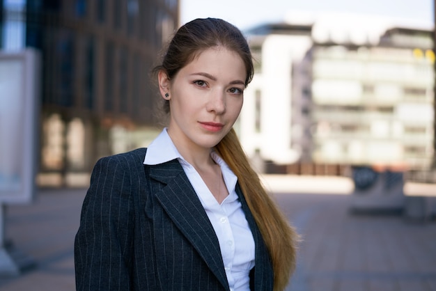 Portret młodej bizneswoman na ulicy w pobliżu centrum biurowego. W czarnej kurtce i białej koszuli