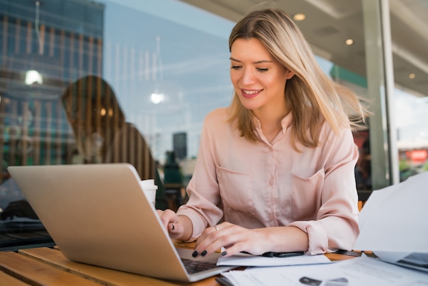 Portret młodej bizneswoman pracuje na swoim laptopie w kawiarni.