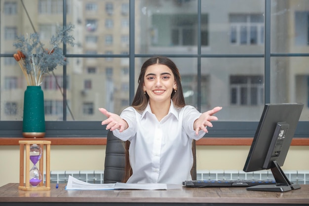 Portret młodej bizneswoman siedzącej przy biurku i wskazującej ręce w stronę kamery