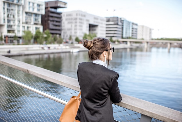 Portret młodej bizneswoman stojącej na moście w nowoczesnej dzielnicy mieszkalnej w Lyonie