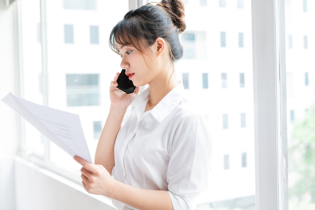 Portret młodej bizneswoman stojącej przy oknie i wykonującej rozmowy telefoniczne ze swoim partnerem