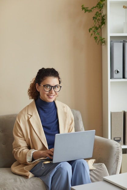 Portret młodej bizneswoman w okularach siedzi na kanapie i pracy online na komputerze przenośnym