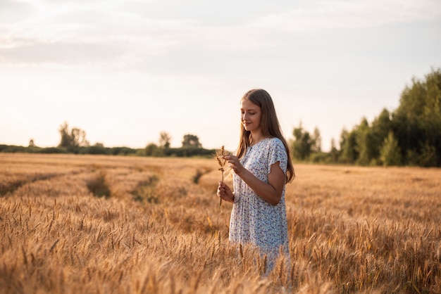 Portret młodej blond dziewczyny z kłosami żyta w dłoniach w polu żyta o zachodzie słońca