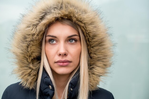 portret młodej blondynki ubrana w zimową kurtkę z kapturem na głowie na białym tle nad białym tłem