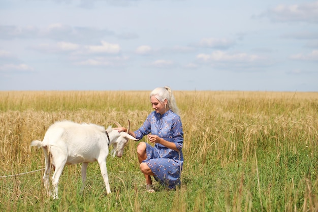 Portret młodej blondynki z kozą na polu pszenicy