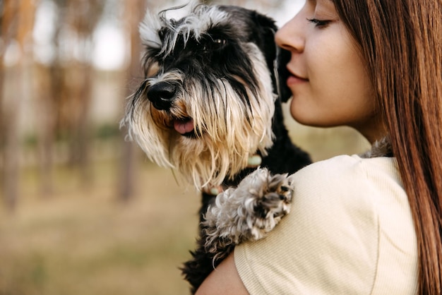 Portret młodej brunetki przytulającej miniaturowego psa rasy schnauzerów