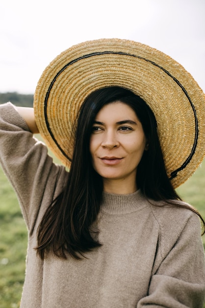 Portret młodej brunetki uśmiechającej się w słomkowym kapeluszu na zewnątrz na polu