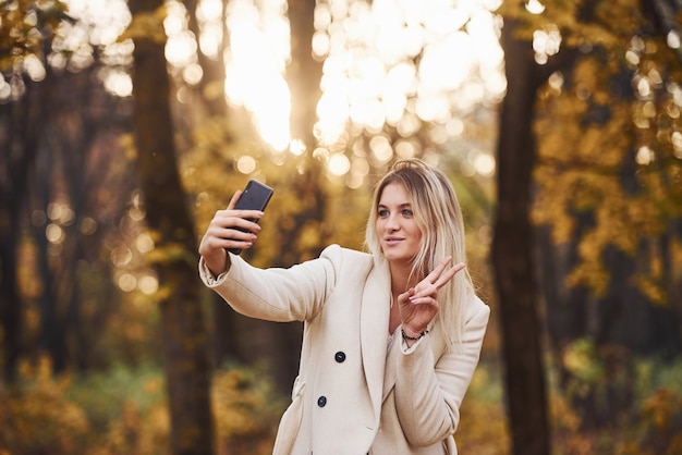 Portret młodej brunetki z telefonem w ręku, który jest w jesiennym lesie w ciągu dnia.