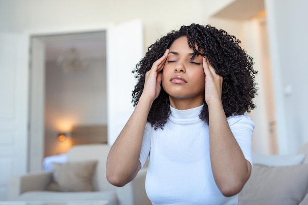 Portret młodej czarnej dziewczyny siedzącej na kanapie w domu z bólem głowy i bólu Piękna kobieta cierpiąca na przewlekłe codzienne bóle głowy Smutna kobieta trzymająca się za głowę z powodu bólu zatok