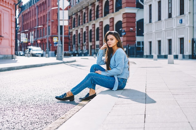 Portret młodej dziewczyny hipster siedzącej na mały odpoczynek podczas spędzania czasu na atrakcyjnej ulicy miasta