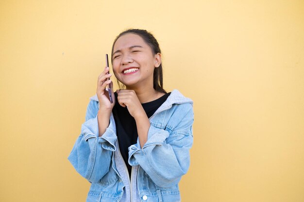 Portret młodej dziewczyny nosi kurtkę dżinsową i używa telefonu komórkowego na brązowym tle