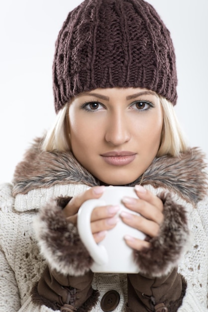 Portret młodej dziewczyny piękne w zimowe ubrania, trzymając w dłoniach filiżankę gorącej herbaty i patrząc na kamery.