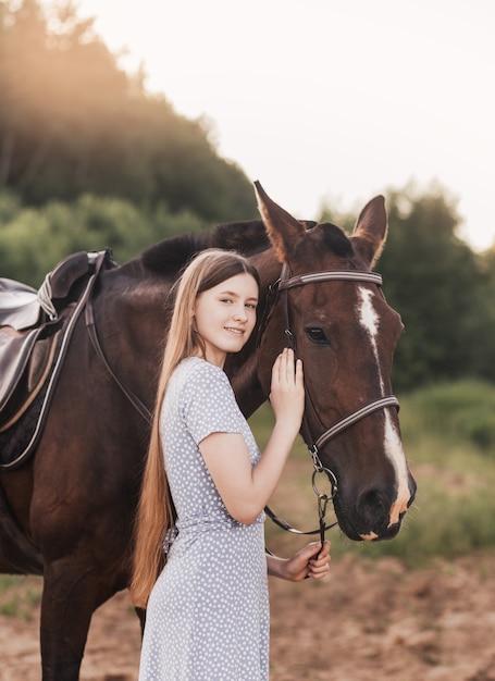 Portret młodej dziewczyny stojącej obok konia patrząc na kamery uśmiechając się.