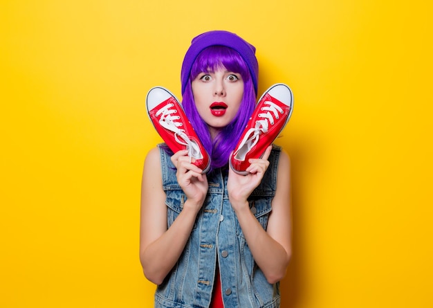 Portret młodej dziewczyny w stylu hipster z fioletowymi włosami i czerwonymi półbutami gumowymi na żółtym tle