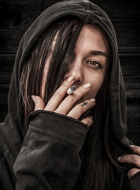Portret młodej dziewczyny z długimi włosami w kapturze, który trzyma w palcach i pali papierosa