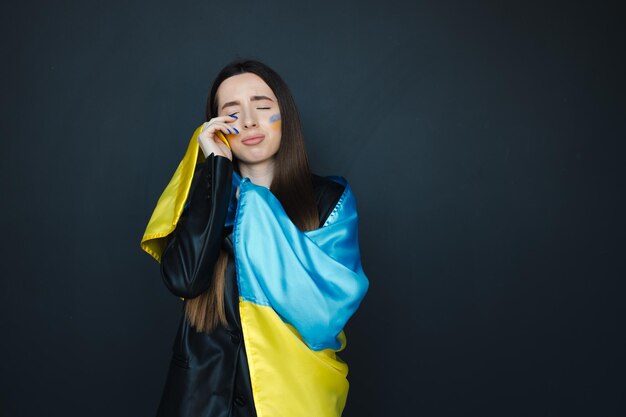 Portret młodej dziewczyny z niebiesko-żółtą flagą Ukrainy na policzku na czarnym tle