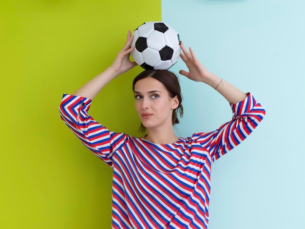 Portret młodej Europejki trzymającej piłkę nożną na głowie. Szczęśliwa dziewczyna, fan piłki nożnej lub gracz odizolowany na zielonym i niebieskim tle. Sport, grać w piłkę nożną, zdrowie, koncepcja zdrowego stylu życia