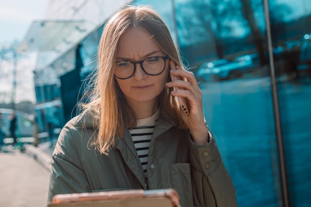 Portret młodej europejskiej blondynki bizneswoman rozmawiającej z telefonem w pobliżu biurowca outd