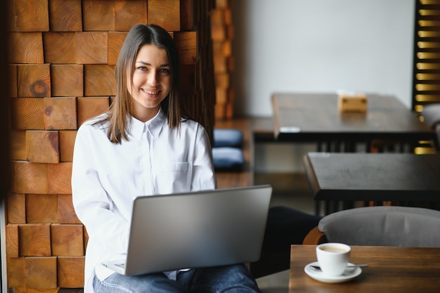 Portret młodej freelancerki korzystającej z laptopa do pracy na odległość, siedząc w nowoczesnym wnętrzu kawiarni, inteligentna blondynka pracująca nad net-bookiem podczas porannego śniadania w kawiarni