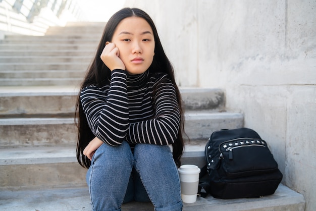Portret młodej kobiety Azji z przemyślanym wyrazem siedzi na betonowych schodach na zewnątrz.