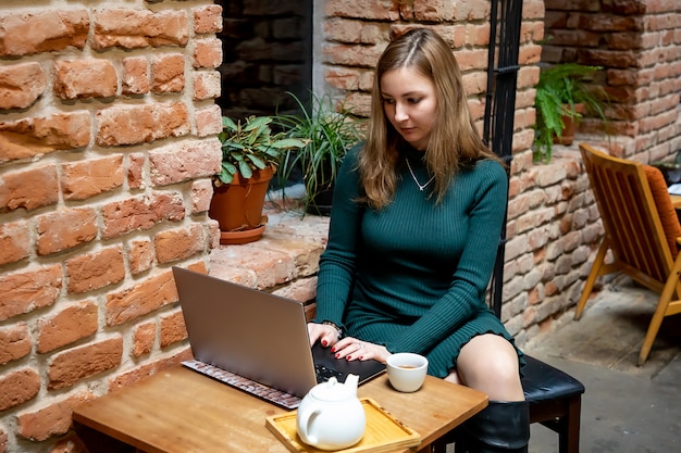 Portret młodej kobiety freelancer używa laptop dla dystansowej pracy podczas gdy siedzący w nowożytnej kawie z filiżanką herbata