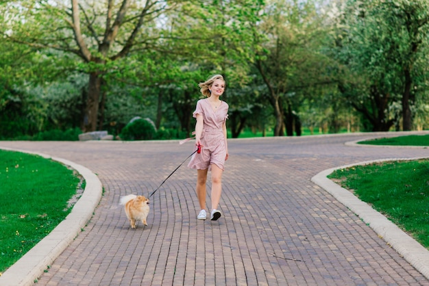 Portret młodej kobiety Glamour noszenie różowej sukience trzyma jej słodkie szpic pomorskim na rękach. . Pojęcie przyjaźni między psami i ludźmi.