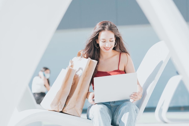 Portret młodej kobiety kupujący sprawdzający swój laptop otoczony torbami szczęśliwy podczas kupowania i przenoszenia toreb na zakupy. Skopiuj miejsce, aktywna koncepcja zakupów. Konsumpcjonizm i sieć społecznościowa młodych ludzi