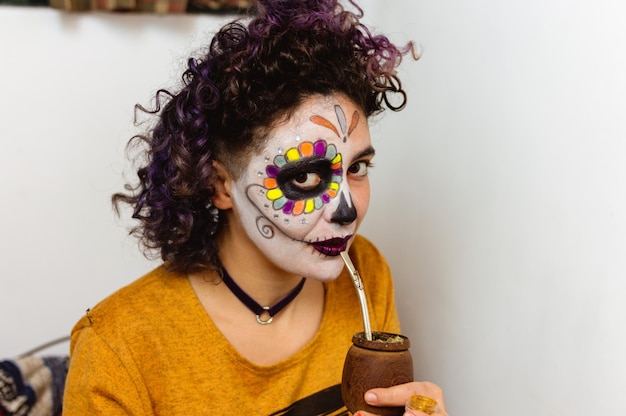 Portret młodej kobiety latynoskiej z makijażem La Calavera Catrina pijąca mate, patrząc w kamerę