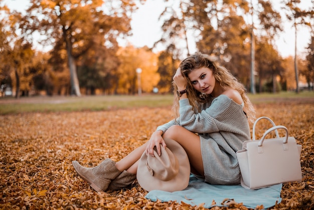 Portret młodej kobiety modne siedzi w parku jesienią.