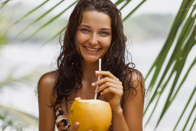 Portret młodej kobiety na plaży w kostiumie kąpielowym z świeżym kokosem na wybrzeżu pod palmą