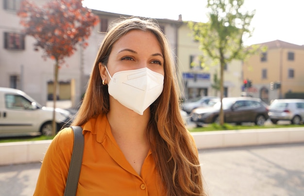 Portret młodej kobiety na ulicy miasta noszącej maskę KN95 FFP2 chroniącą przed rozprzestrzenianiem się wirusa SARS-CoV-2. Dziewczyna z maską ochronną na twarzy przeciwko chorobie koronawirusowej 2019.