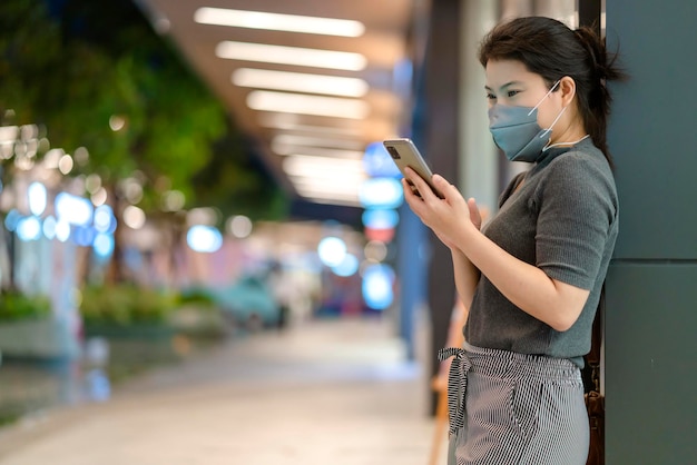 Portret młodej kobiety noszącej maskę ochronną na twarz, aby zapobiec rozprzestrzenianiu się wirusa, ręcznie używać technologii smartfonów, komunikacji, nowej koncepcji normalnego stylu życia