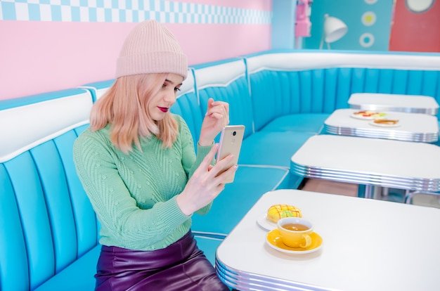 Portret młodej kobiety obsiadanie przy kawiarnią i używać telefon komórkowego