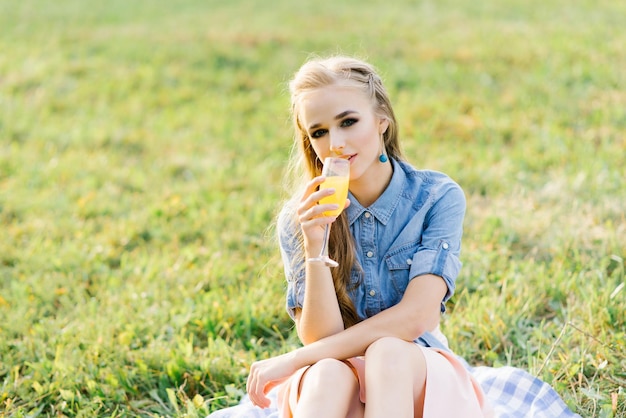 Portret młodej kobiety pijącej sok pomarańczowy w szklance na letnim pikniku w parku
