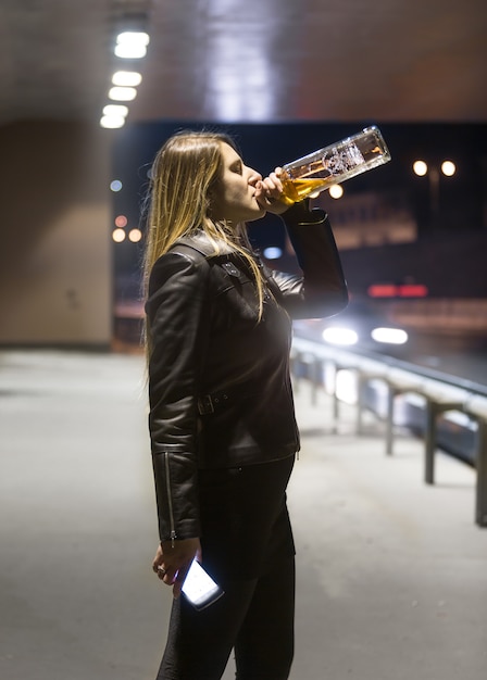 Portret młodej kobiety pijącej whisky z butelki i nocy