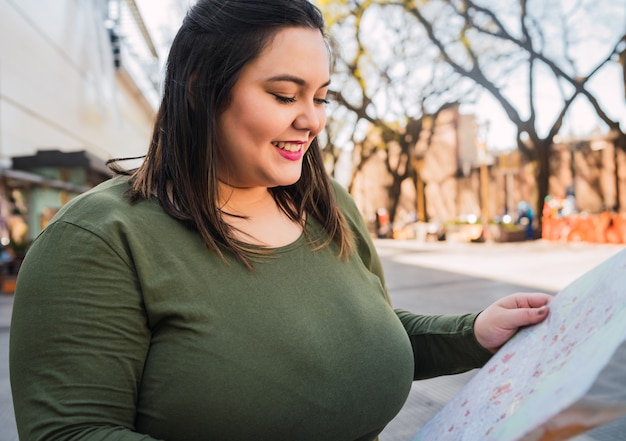 Zdjęcie portret młodej kobiety plus size trzymającej mapę i szukającej wskazówek na zewnątrz na ulicy