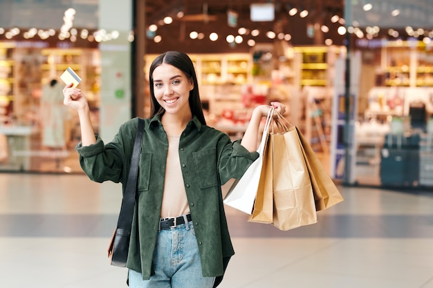 Portret młodej kobiety podekscytowany z torby papierowe przy użyciu karty kredytowej podczas zakupów w centrum handlowym