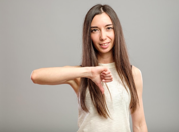 Portret młodej kobiety pokazującej gest kciuka w dół na szarym tle