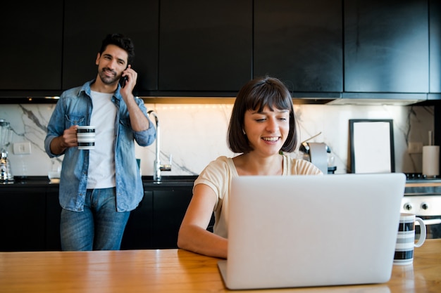 Portret młodej kobiety pracy z laptopem w domu, podczas gdy mężczyzna rozmawia przez telefon
