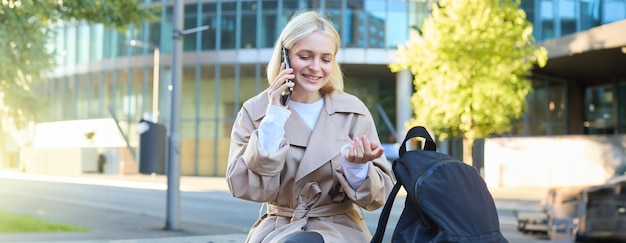 Portret młodej kobiety siedzącej na ławce, rozmawiającej przez telefon komórkowy, spędzającej czas na zewnątrz.