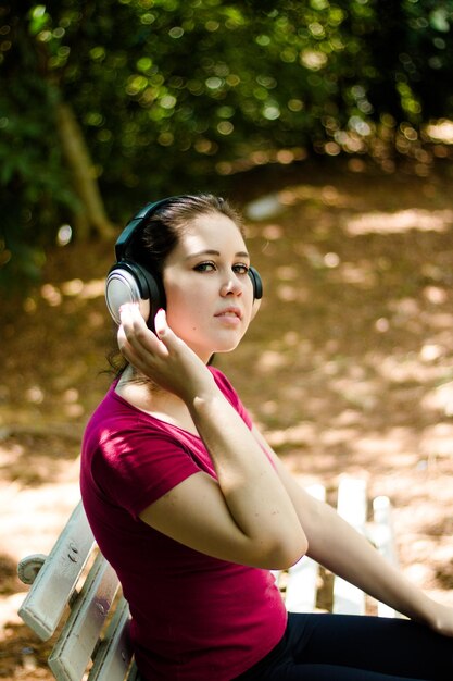 Portret młodej kobiety słuchającej muzyki siedzącej na ławce w parku