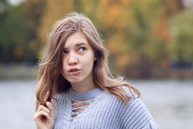 Portret młodej kobiety śmieszne patrząc w górę i gryząc wargę z zamyślonym spojrzeniem w parku