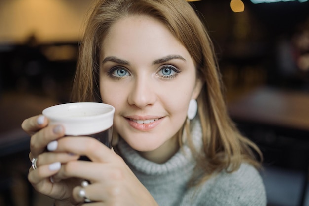 Zdjęcie portret młodej kobiety trzymającej kawę siedzącej w kawiarni