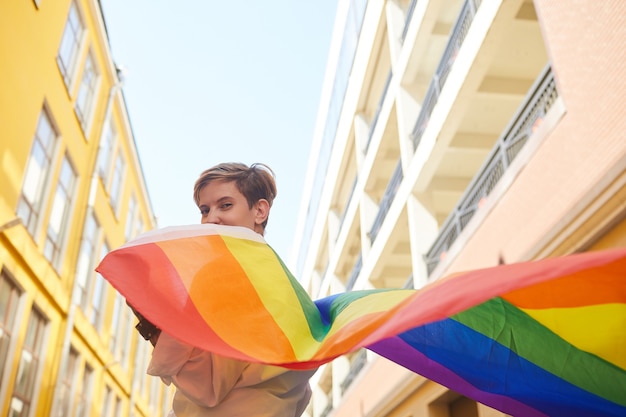 Portret młodej kobiety trzymającej kolorową flagę, jest w lesbijskiej paradzie w mieście