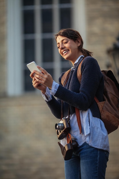 Portret młodej kobiety trzymającej telefon komórkowy podczas zwiedzania obcego miasta