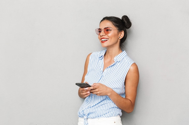 Portret Młodej Kobiety Uśmiechnięta W Okulary Odizolowane, Przy Użyciu Telefonu Komórkowego