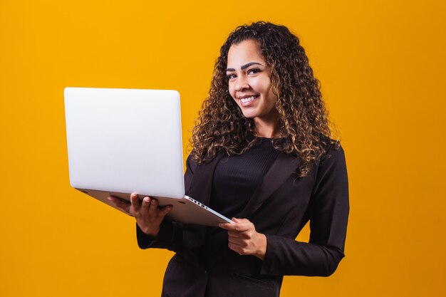 Portret młodej kobiety w stroju wykonawczym z laptopem na żółtym tle. Kobieta pracuje z laptopem